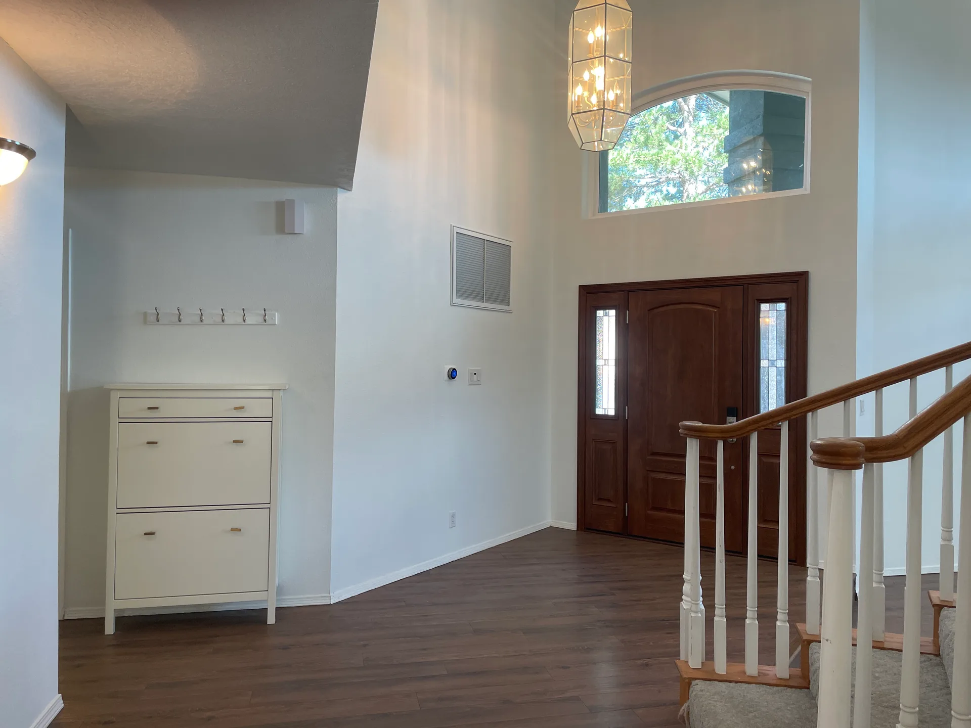 Home foyer entryway with high ceilings, wood-style flooring, and a staircase with white spindles