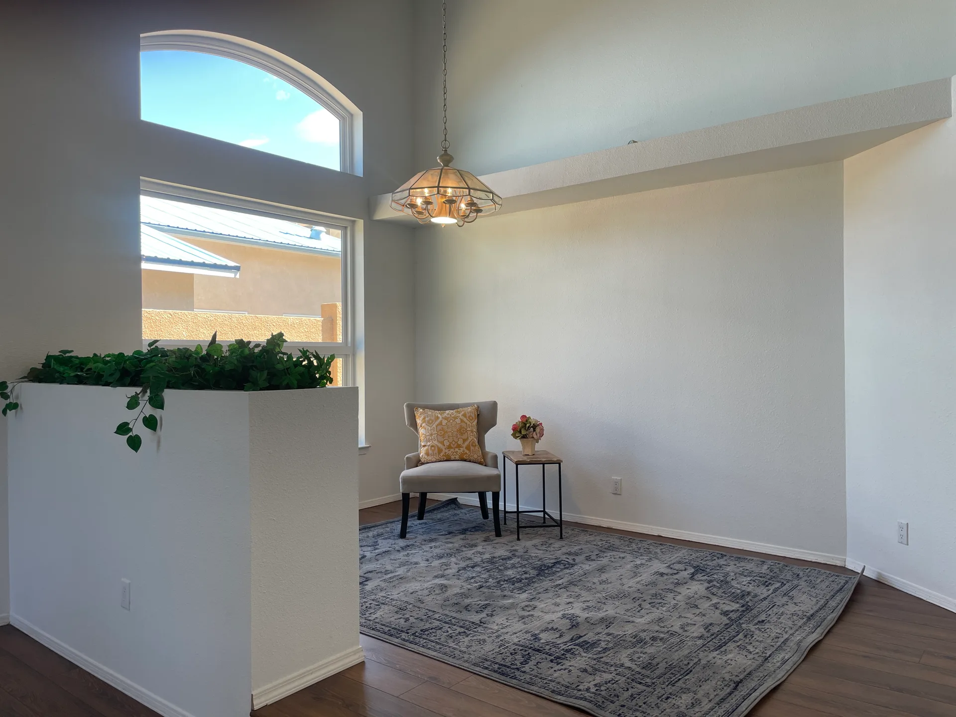 Living room with vaulted ceilings, laminate flooring, and a tall arched window