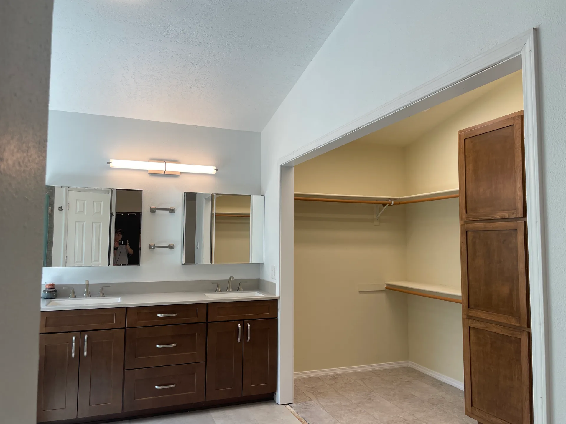 Master bathroom with double vanity, wood cabinetry, vaulted ceiling, and walk-in closet