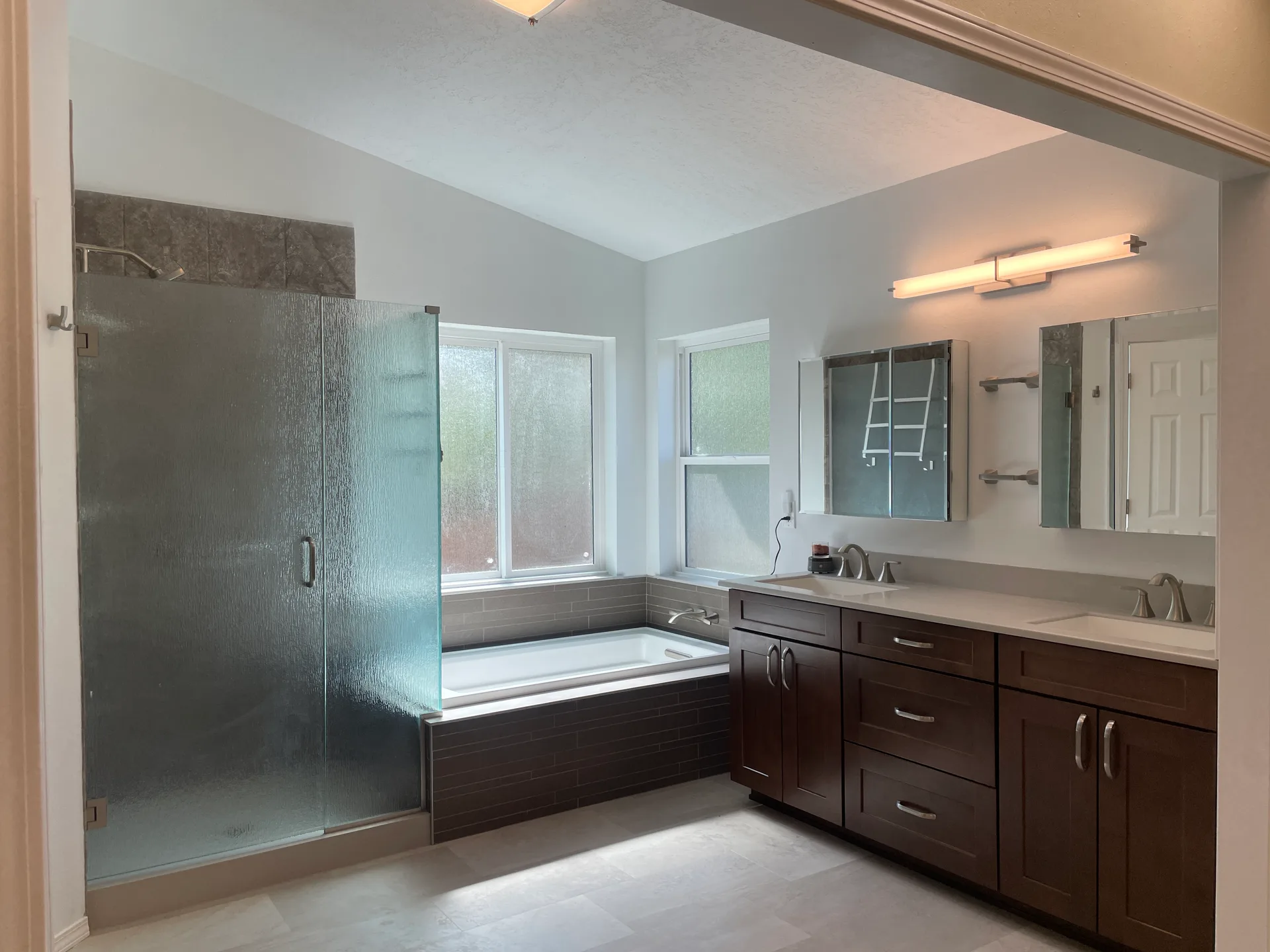 Primary bathroom with dual-sink dark wood vanity, soaking tub, and glass-enclosed shower
