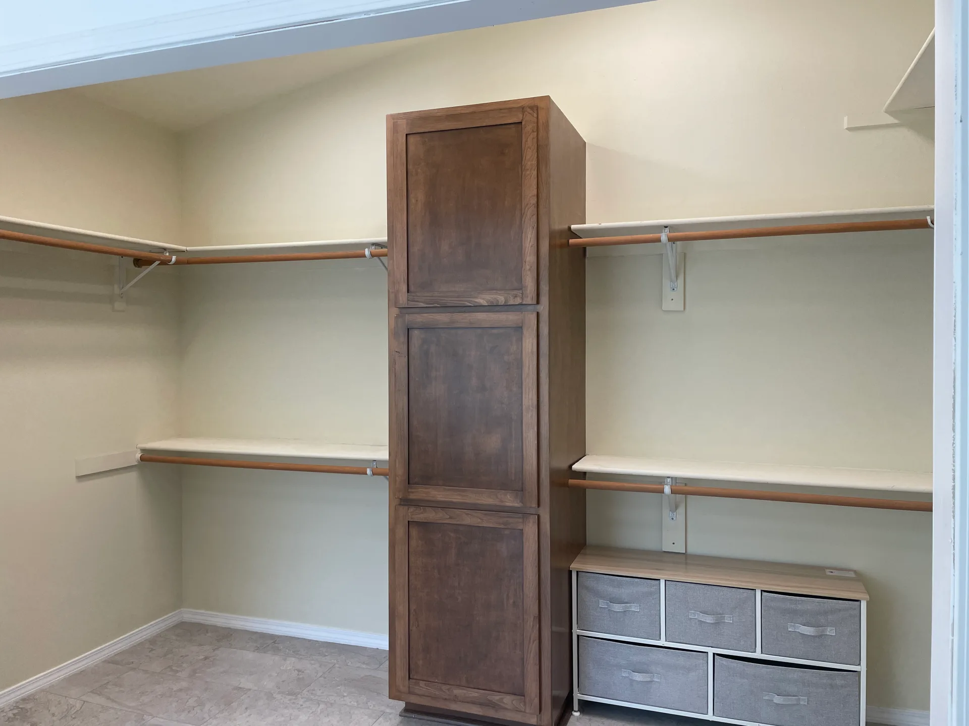 Walk-in master closet with wood-stained cabinetry, white shelving, and hanging rods