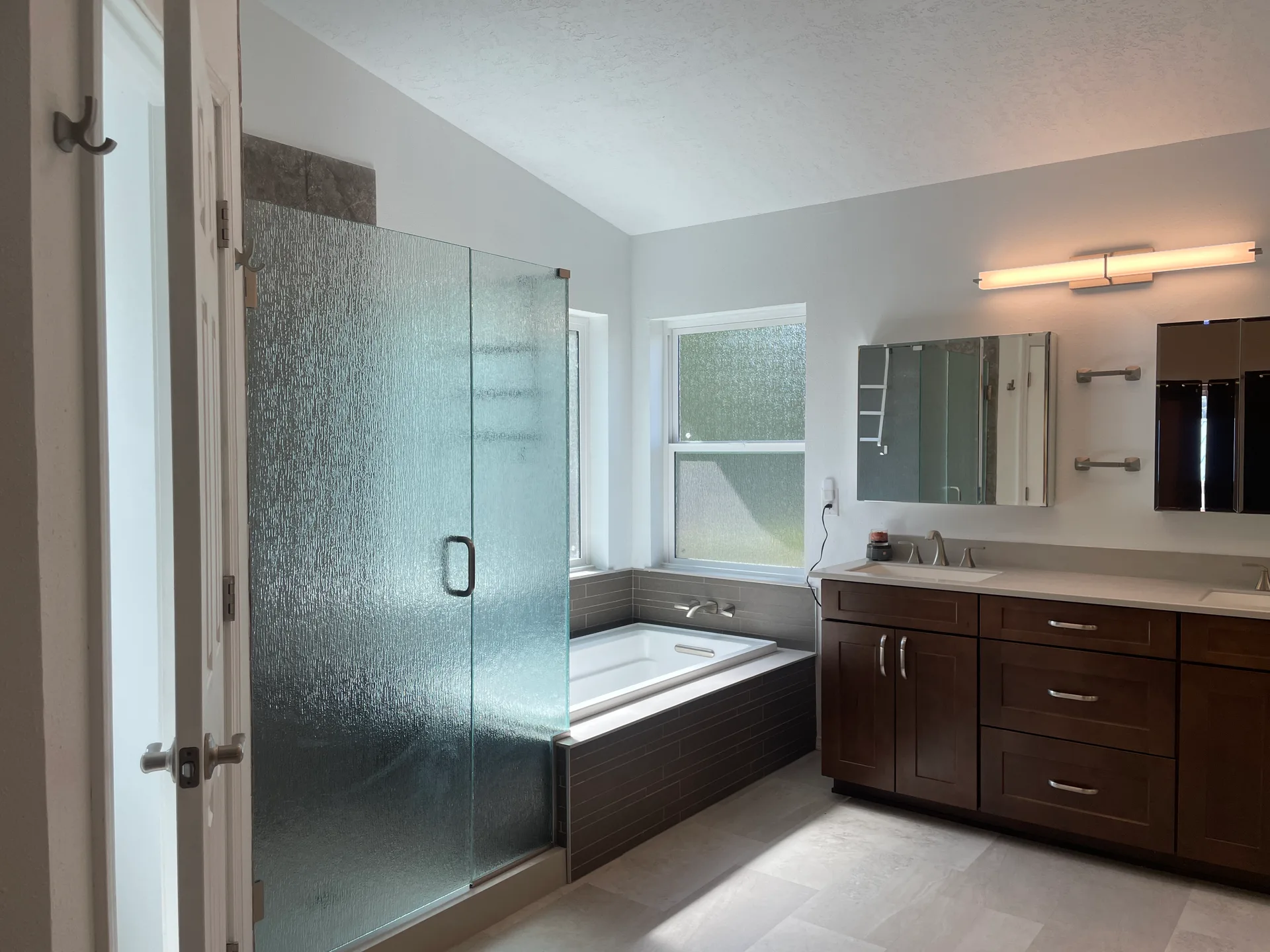 Primary bathroom with dark wood vanity, stone-tiled tub deck, and glass shower enclosure