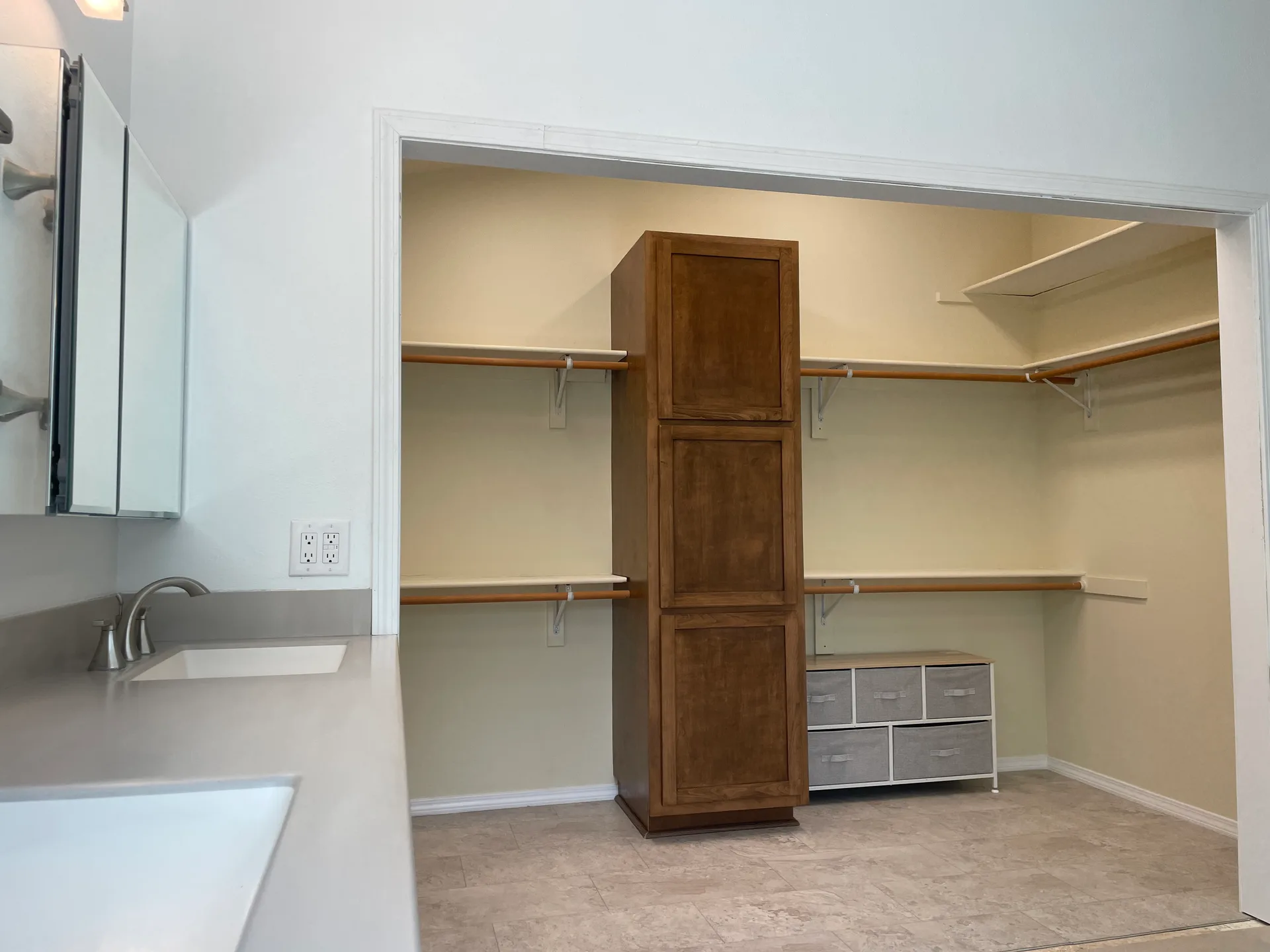 Bathroom with dual white sinks, dark wood cabinetry in closet, and stone-look countertops