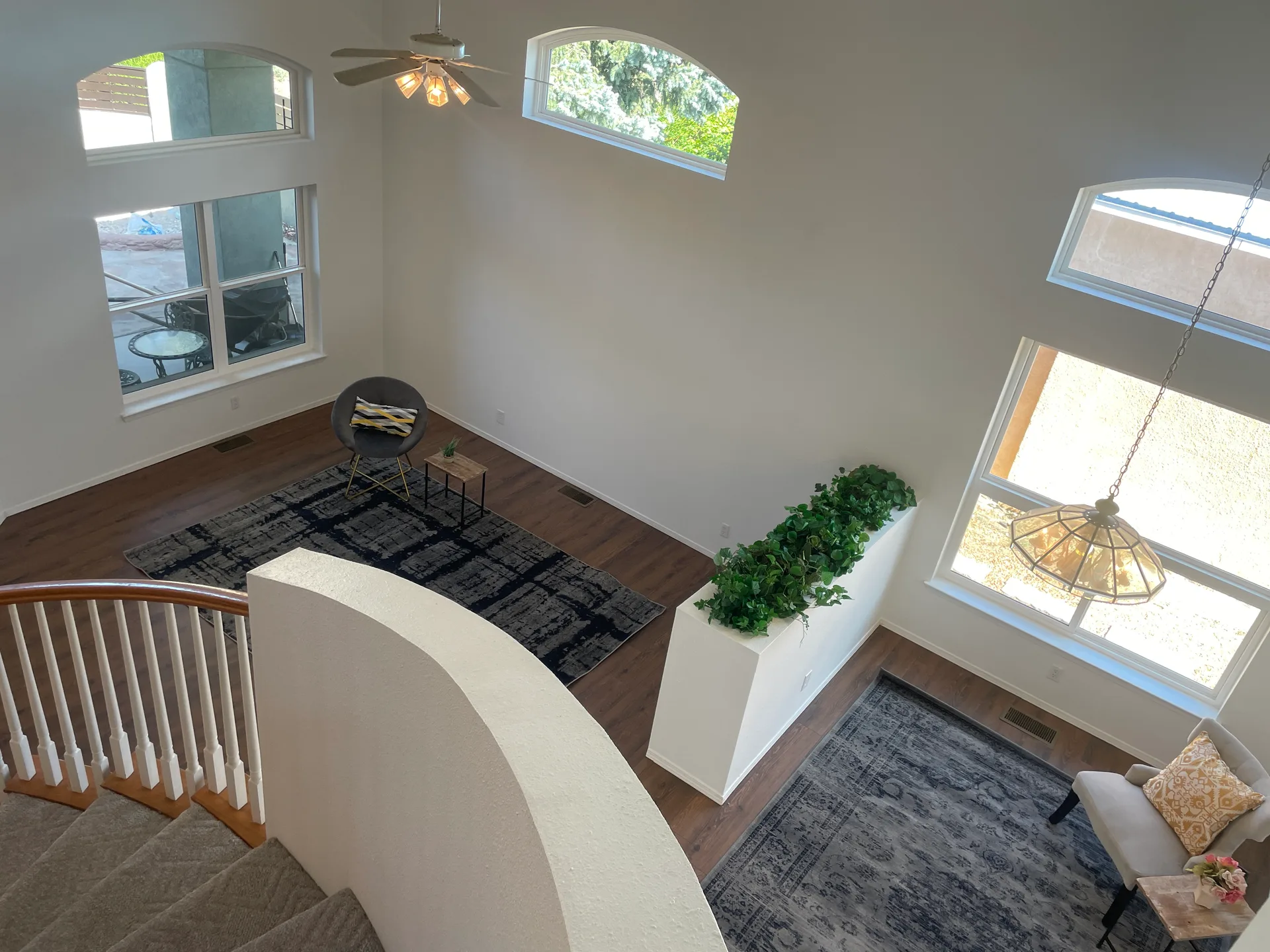 Living room view from the staircase showing vaulted ceilings, arched windows, and wood flooring