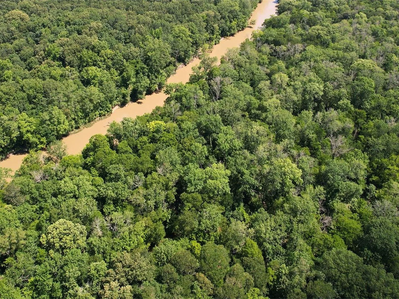 Aerial drone of dense wooded acreage and flowing river