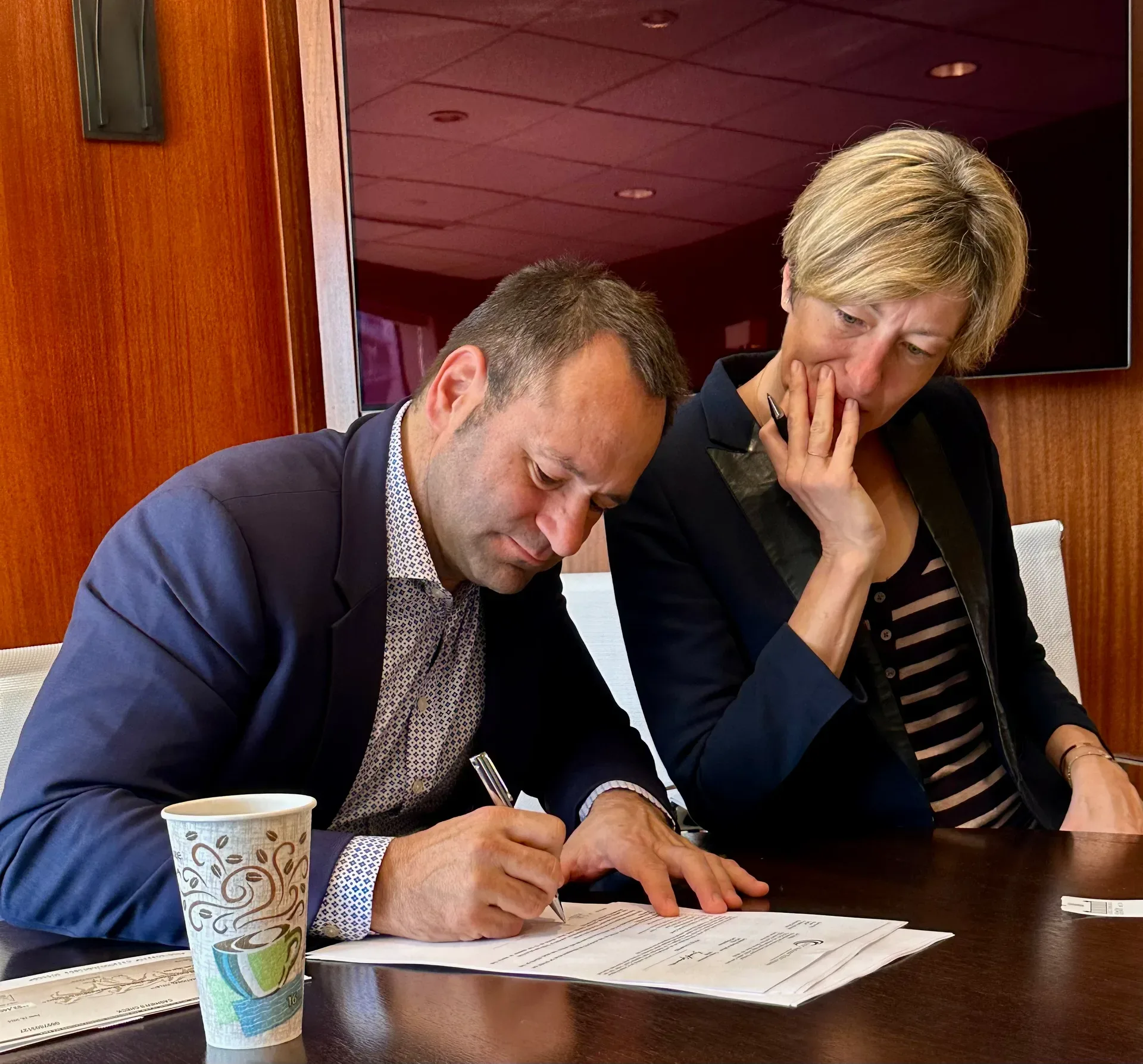 A man signing closing documents with a woman looking on in a professional office setting