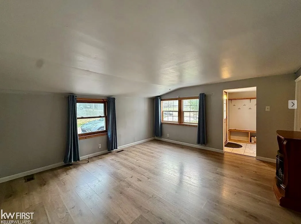 Living room interior showing light wood-look flooring and windows with natural light