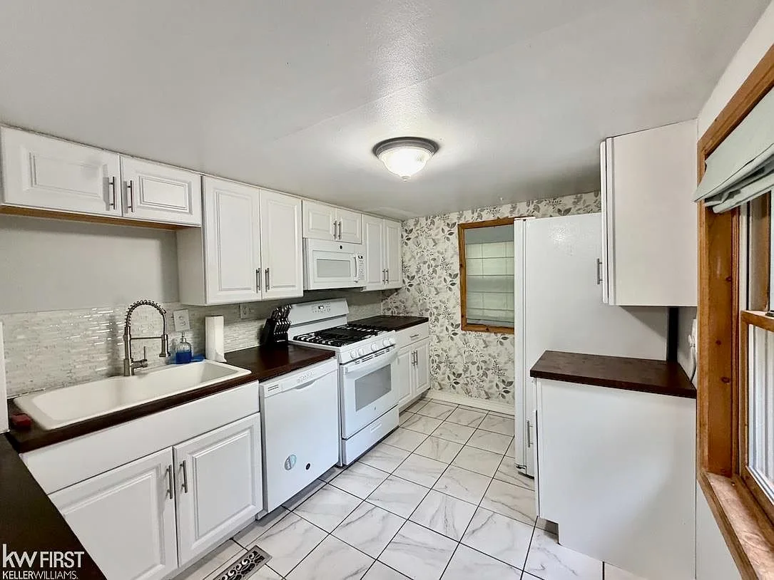 Wide-angle kitchen view showing white cabinetry, dark countertops, and floral wallpaper accent