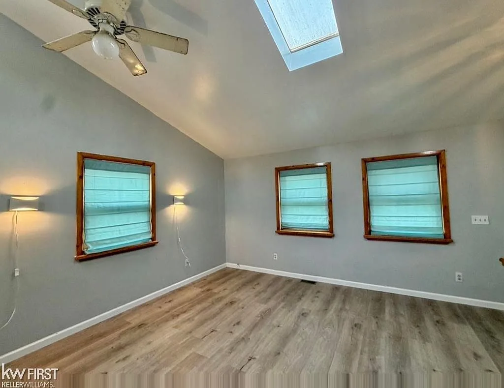Master bedroom showing vaulted ceiling, skylight, and teal roman shades