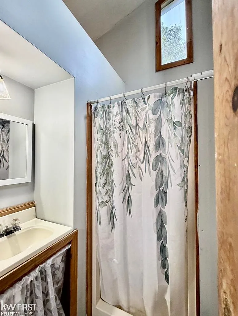 Bathroom with vanity, sink, mirror, and shower area