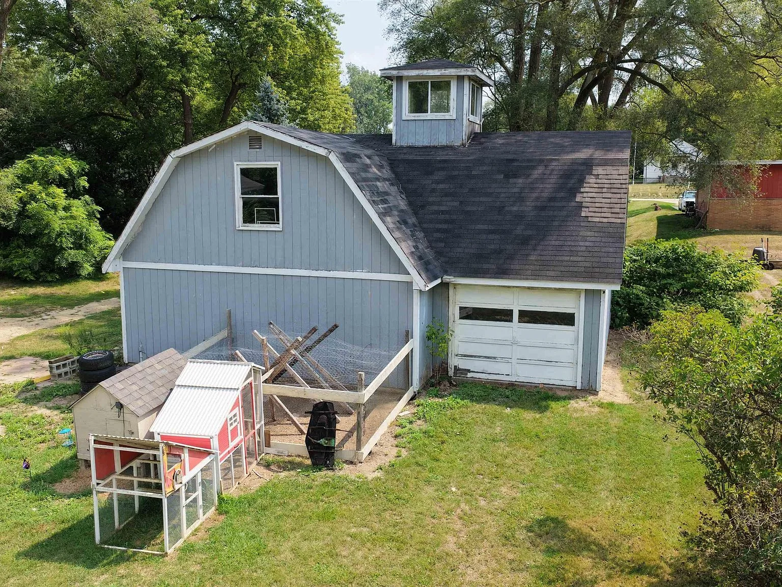 Detached building with gambrel roof, grey vertical siding, cupola, and garage door