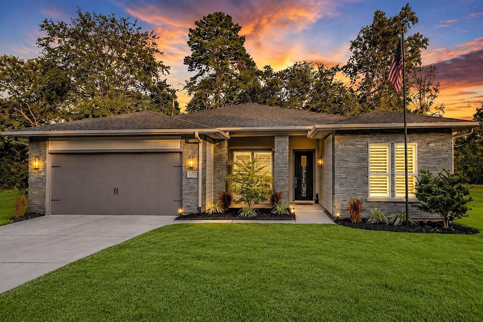 Front exterior of 15714 Corinthian Way at sunset, a one-story home for sale in Corinthian Point with stone veneer, dark garage door, and manicured lawn