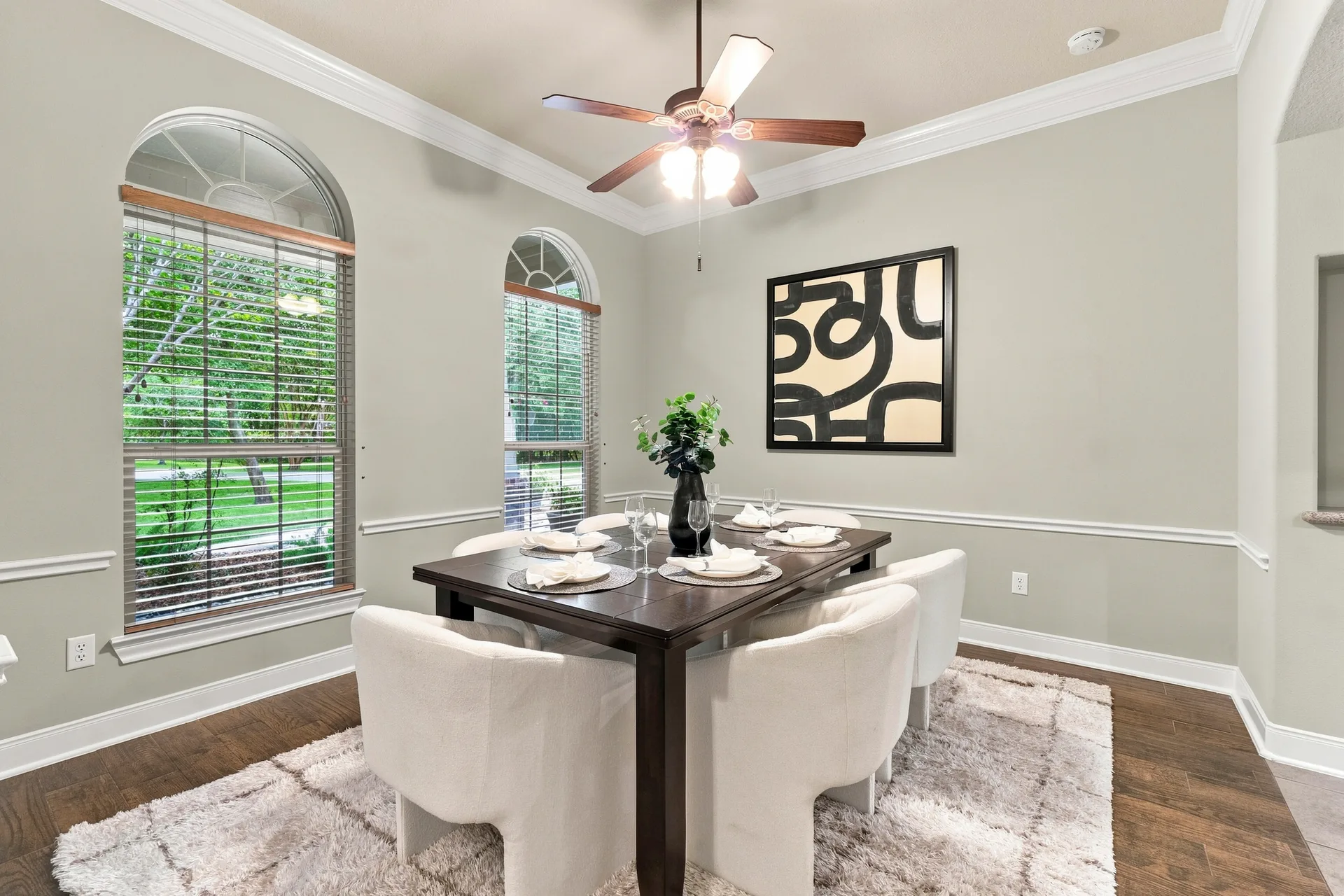Formal dining room with dark wood table, white upholstered chairs, and arched windows with blinds