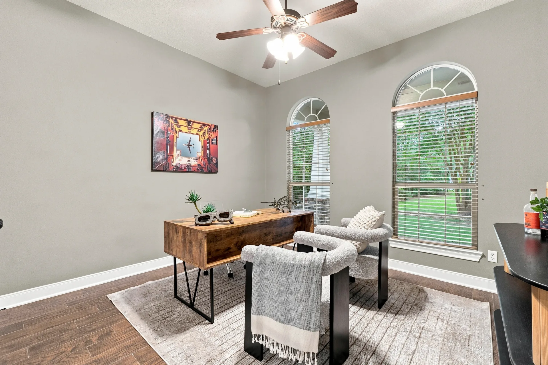 Home office or study with wood-look floors, grey walls, and arched windows with natural daylight