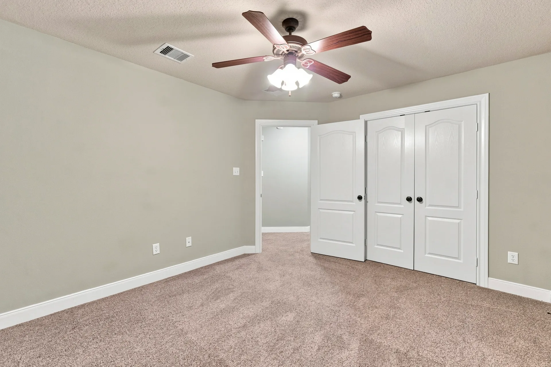 Bedroom with neutral beige walls, light carpet, white trim, and bright interior lighting