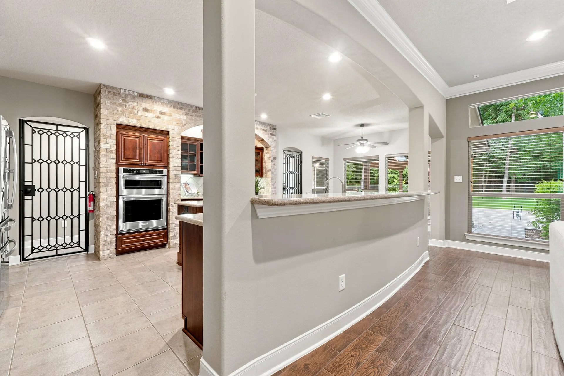 Kitchen and living area transition with wood cabinetry, brick veneer accents, and tile and wood flooring