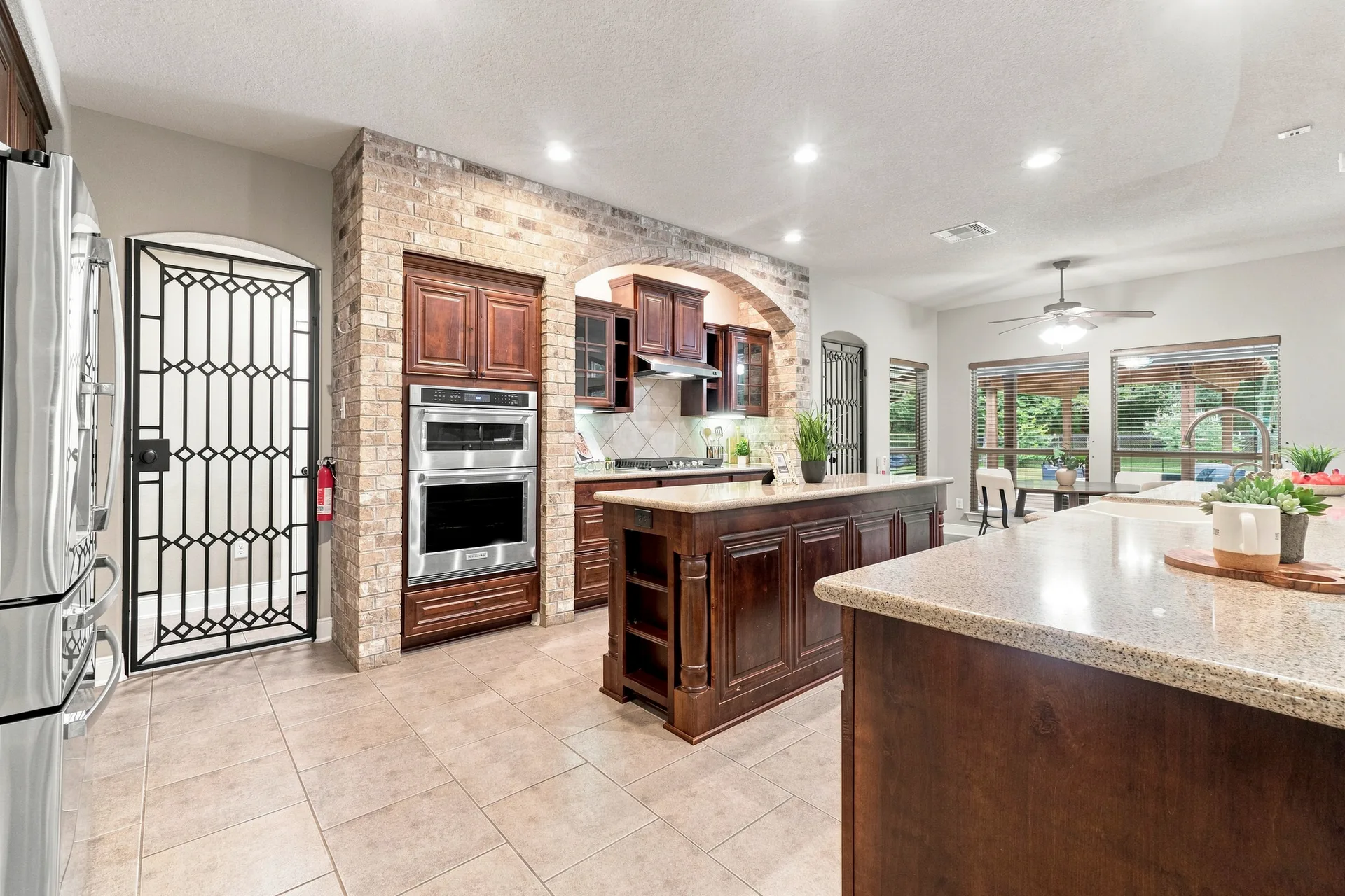 Wide-angle kitchen with dark wood cabinetry, brick-encased double oven, granite countertops, and tile flooring