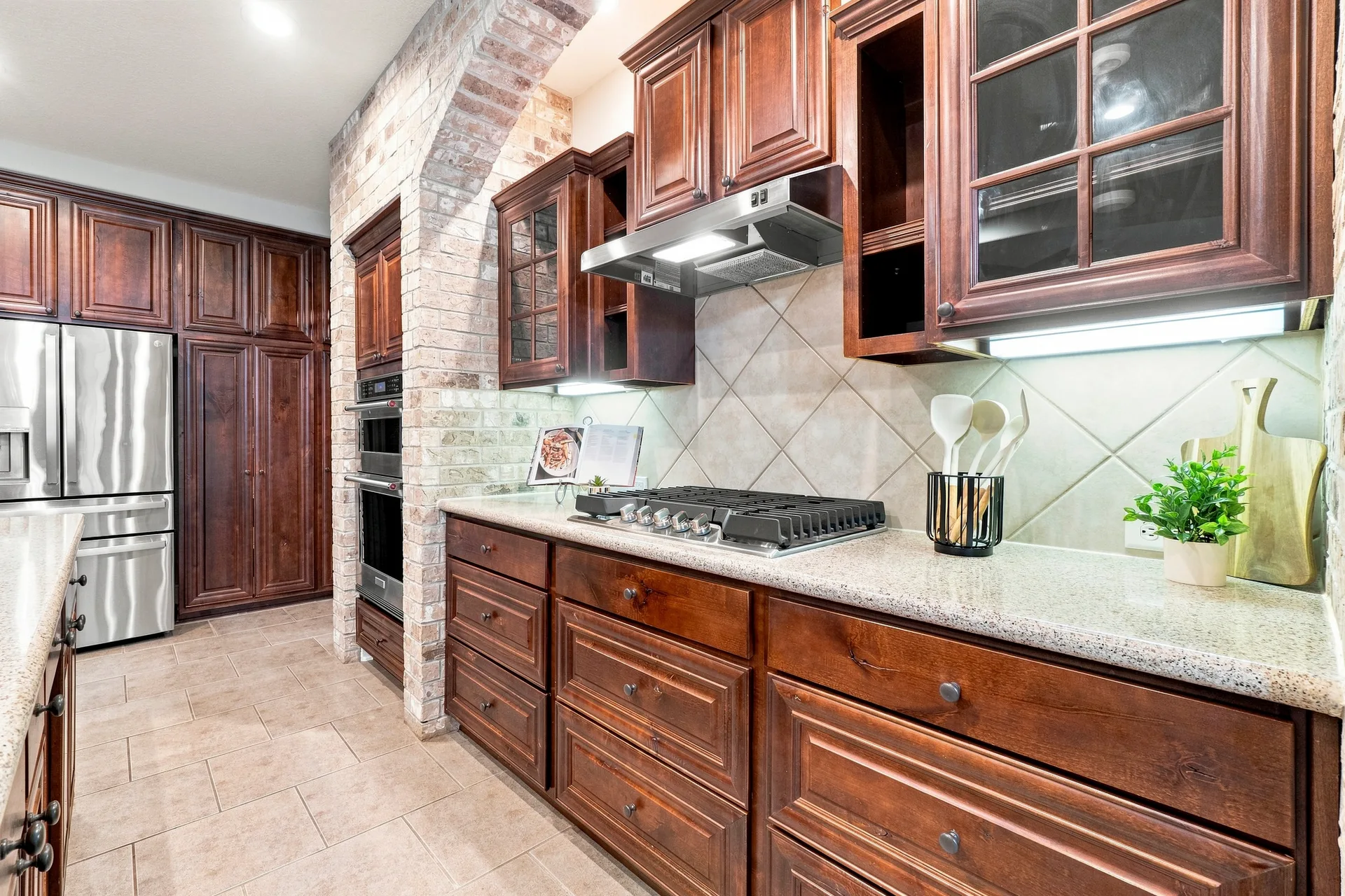 Kitchen cooking area with dark wood cabinets, brick-enclosed oven niche, gas cooktop, and granite countertops