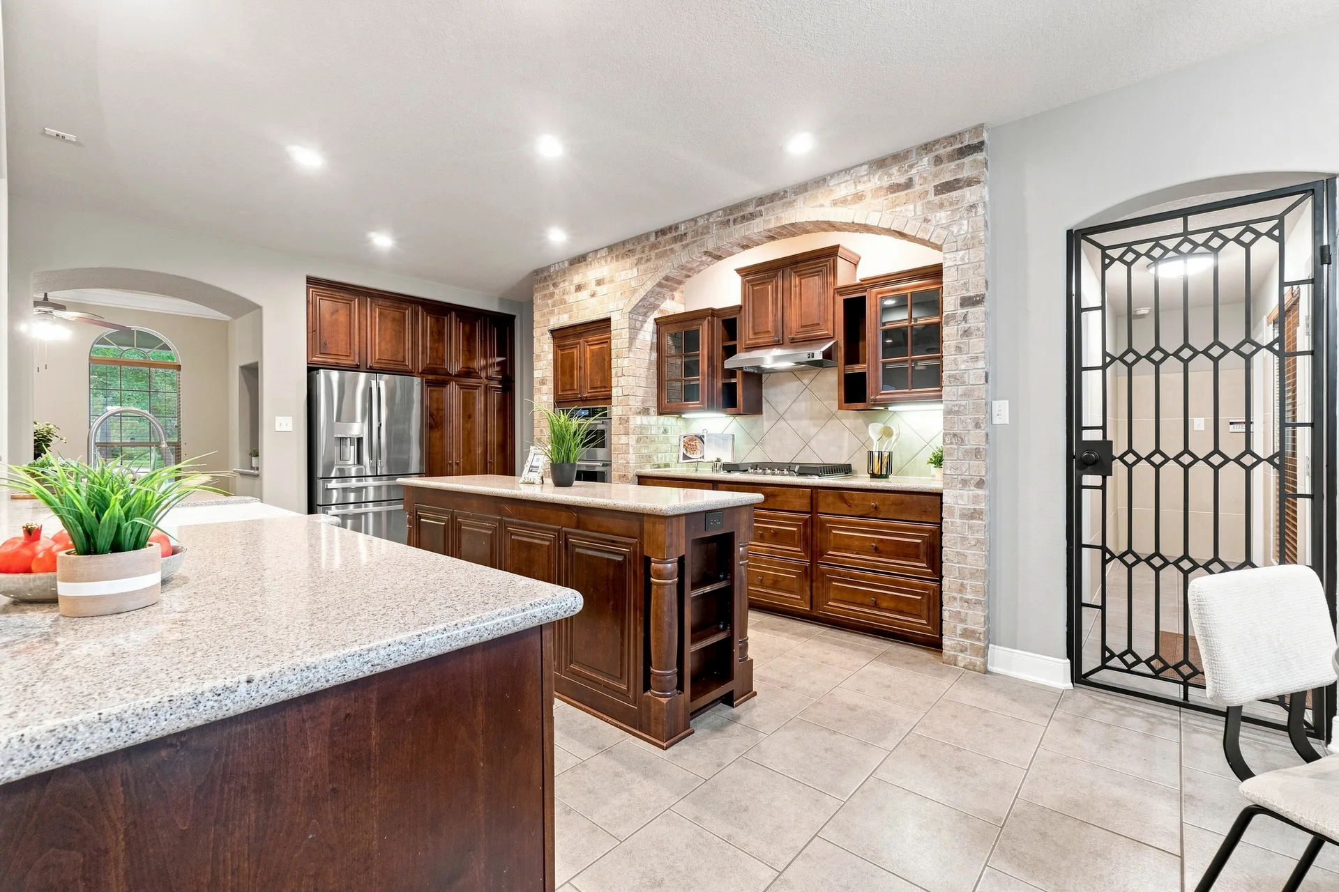 Kitchen with dark wood cabinetry, brick arch feature above the cooktop, granite countertops, and tile flooring