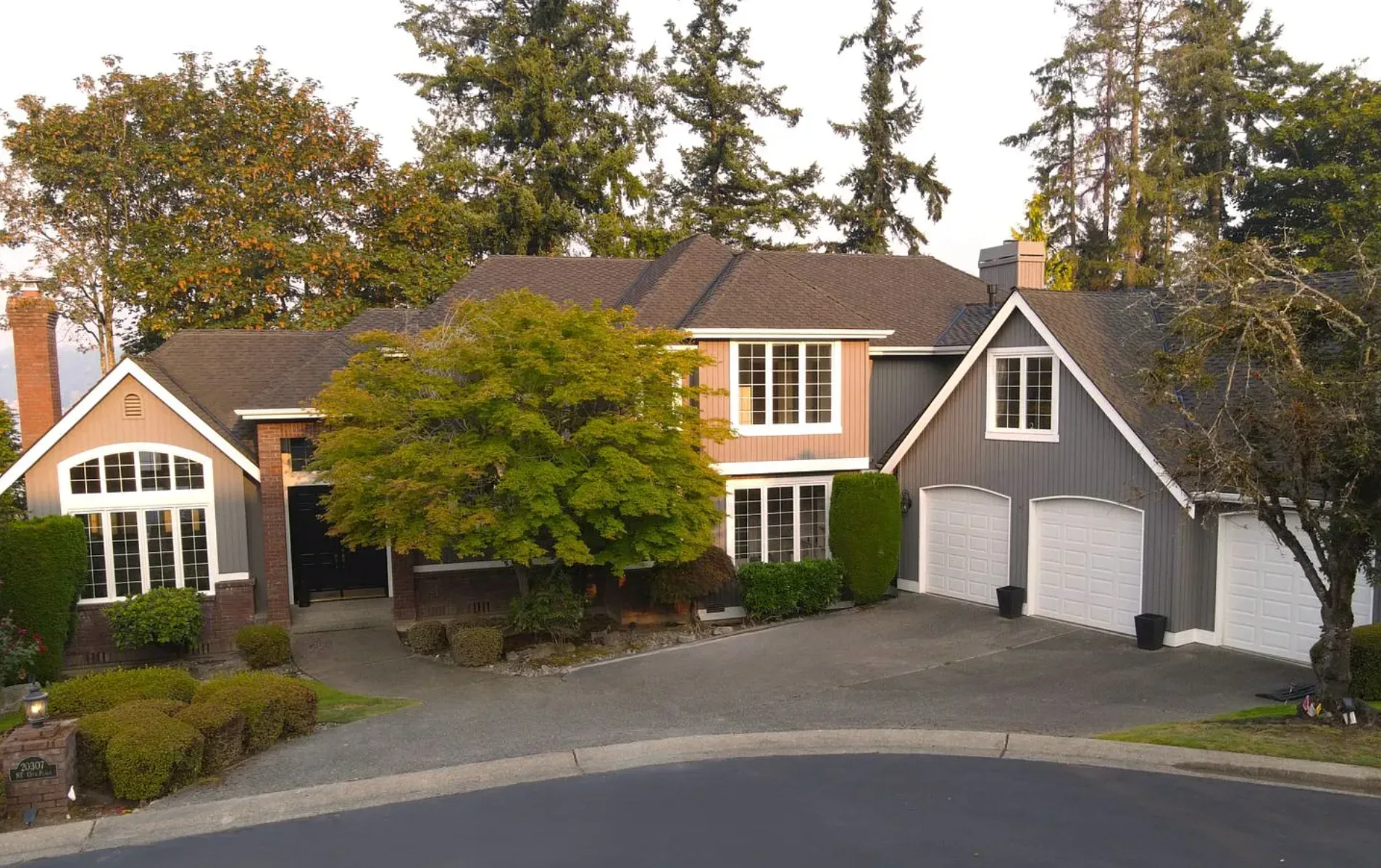 Traditional Sammamish home with brick and grey wood-paneled siding, three-car garage, and mature trees in a suburban setting