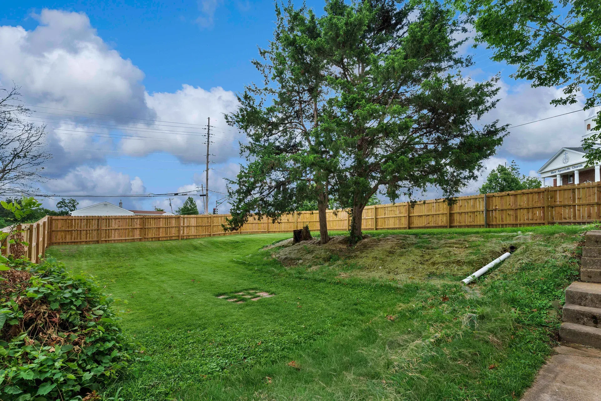 Sloped fenced backyard with mature trees and privacy fence