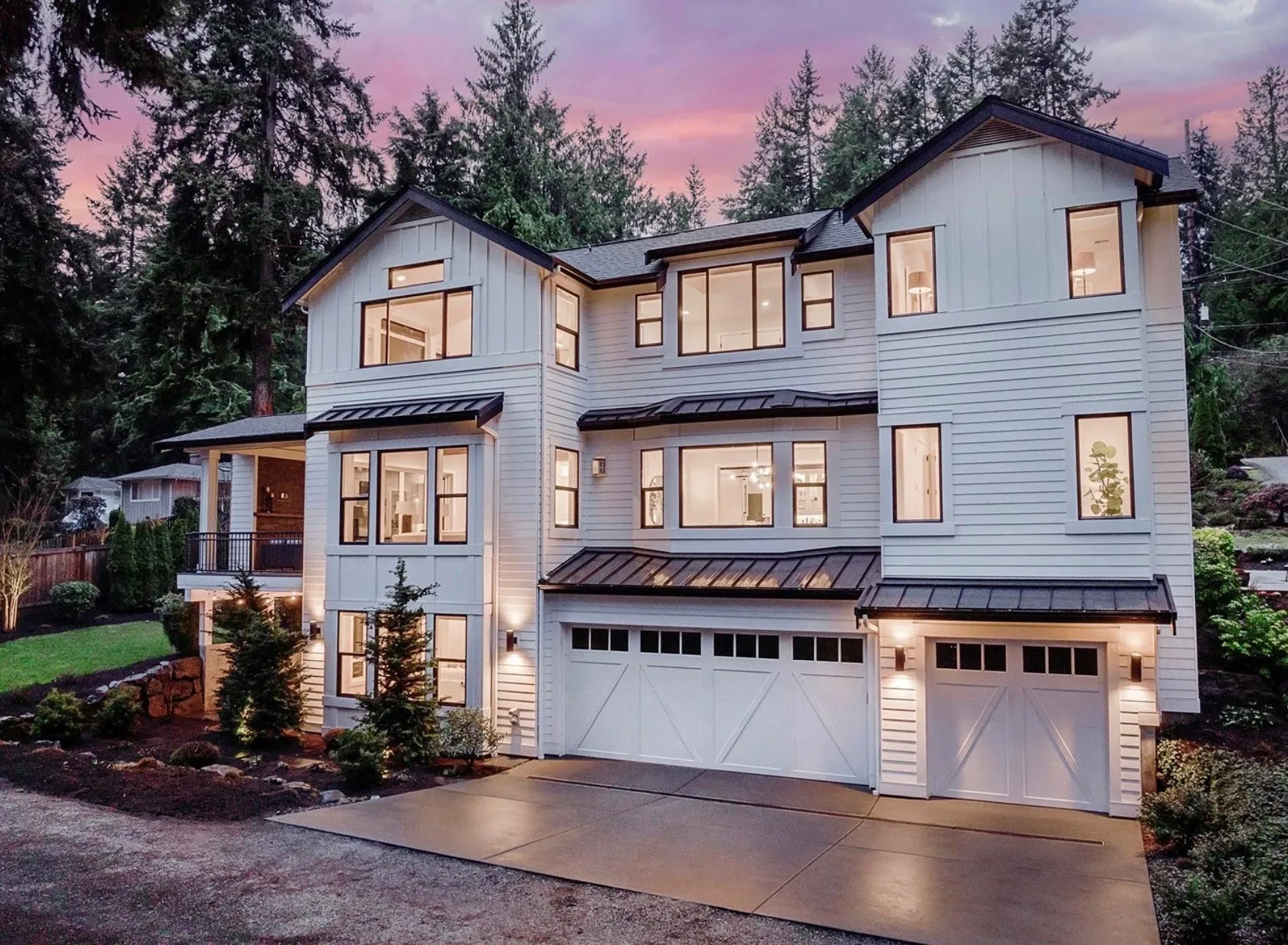 White modern farmhouse with black trim, multi-car garage, and mature trees at dusk