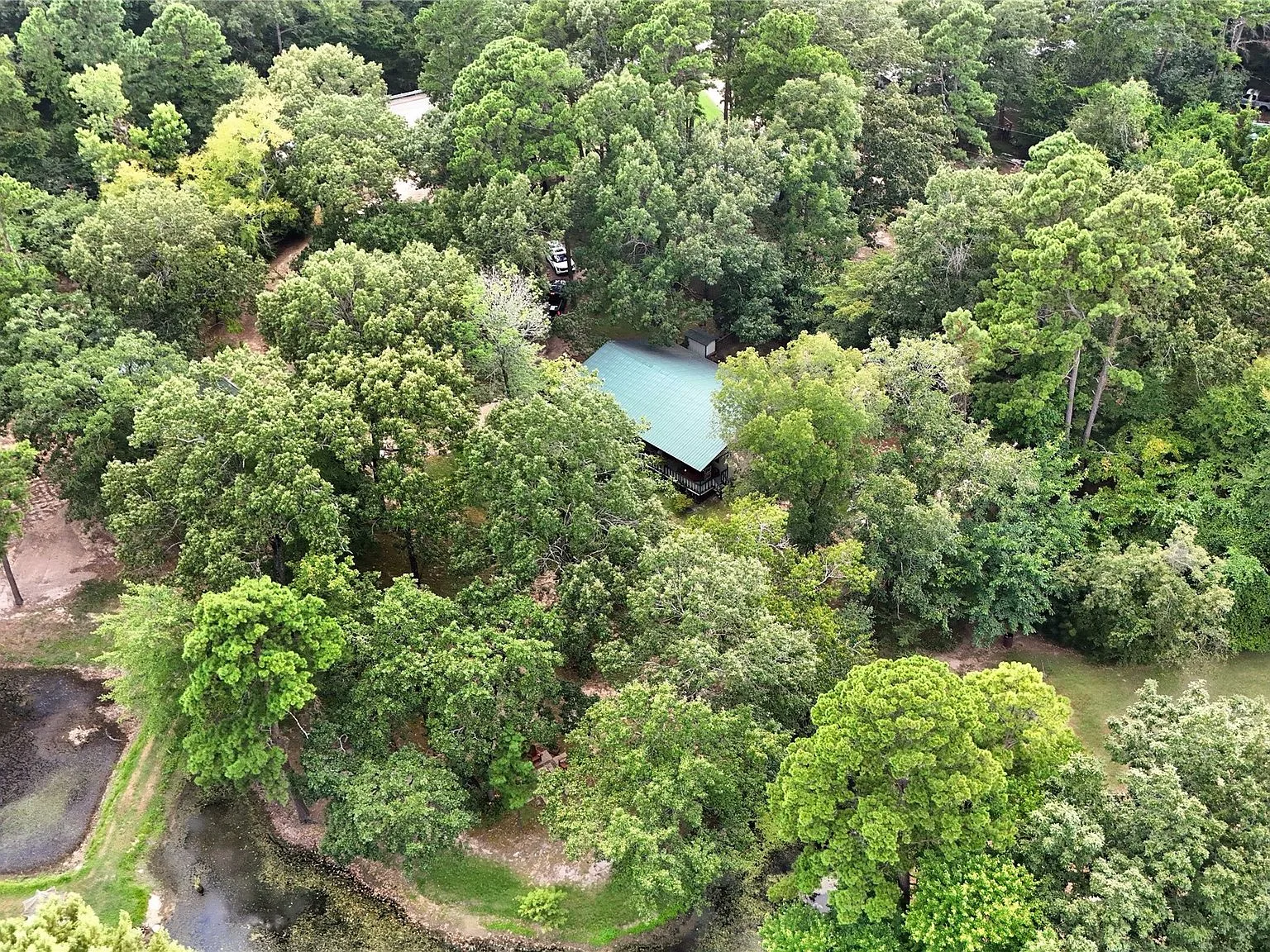 Aerial drone photograph of the ranch home at 1308 FM 906 W, Powderly TX nestled among dense trees, showing the wooded seclusion of the 1.5-acre property