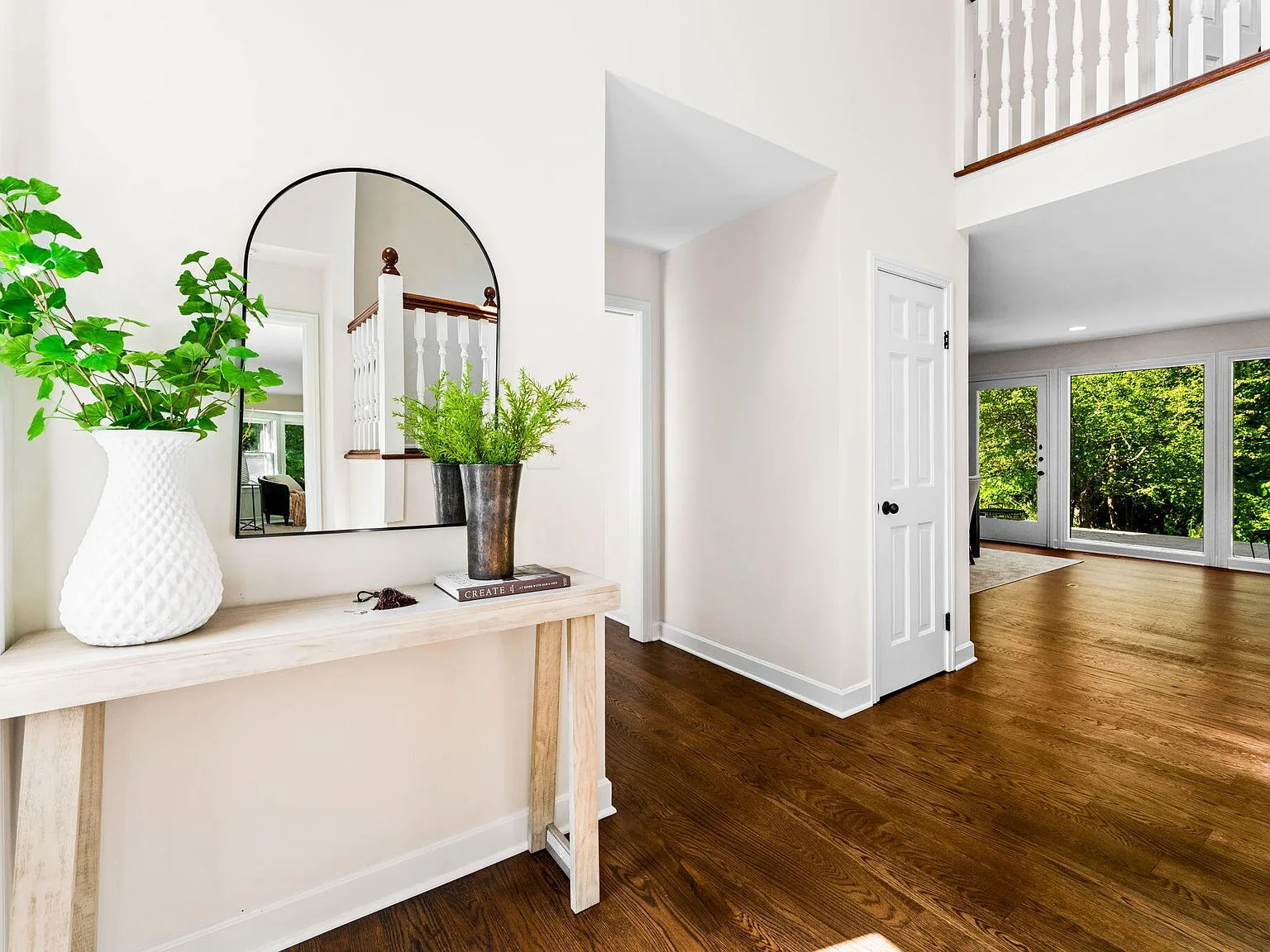 Foyer entrance with hardwood floors, white trim, and arched mirror