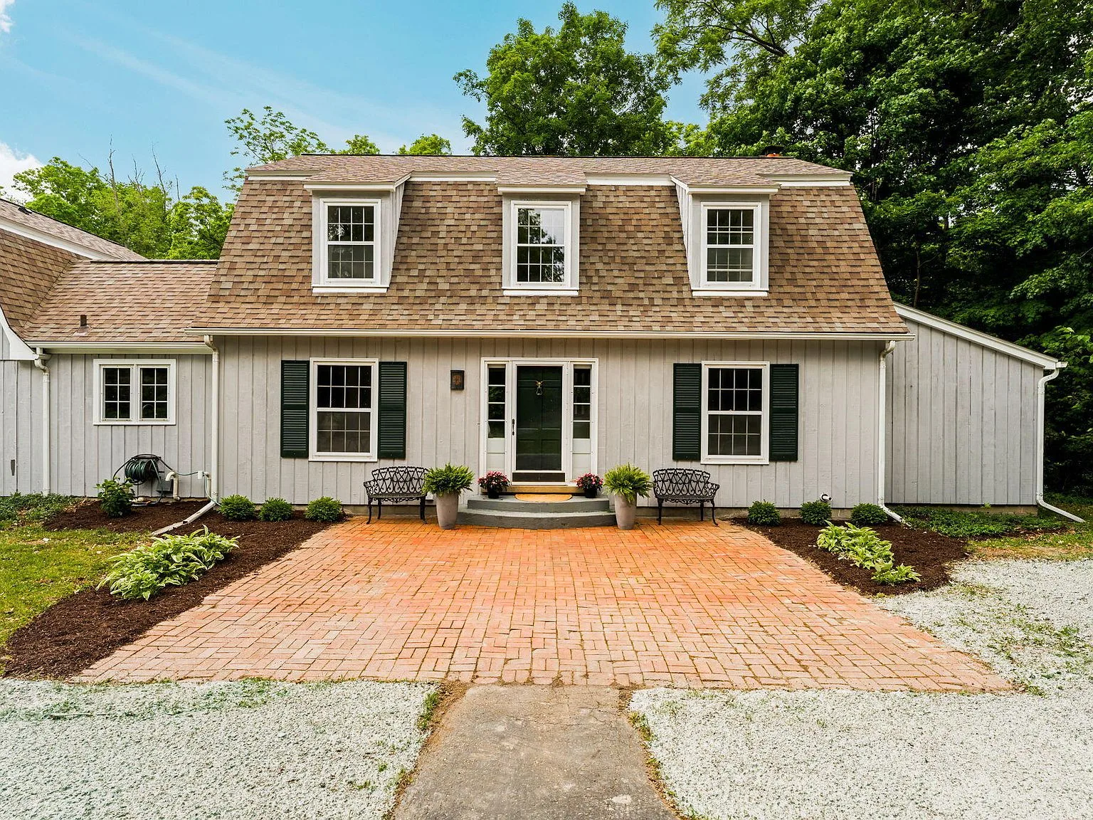 Front facade of 5175 Dixboro Rd, a gambrel-roofed estate home with grey vertical siding and brick patio