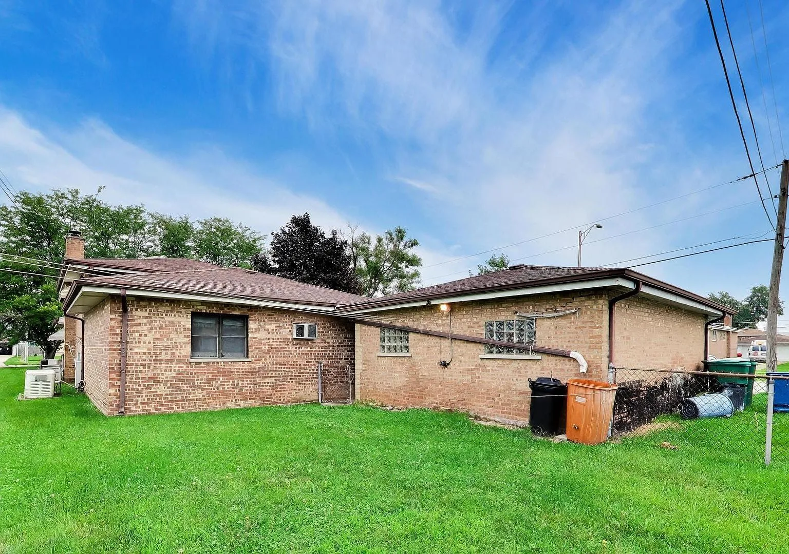 Backyard view of brick home with green lawn and chain-link fence