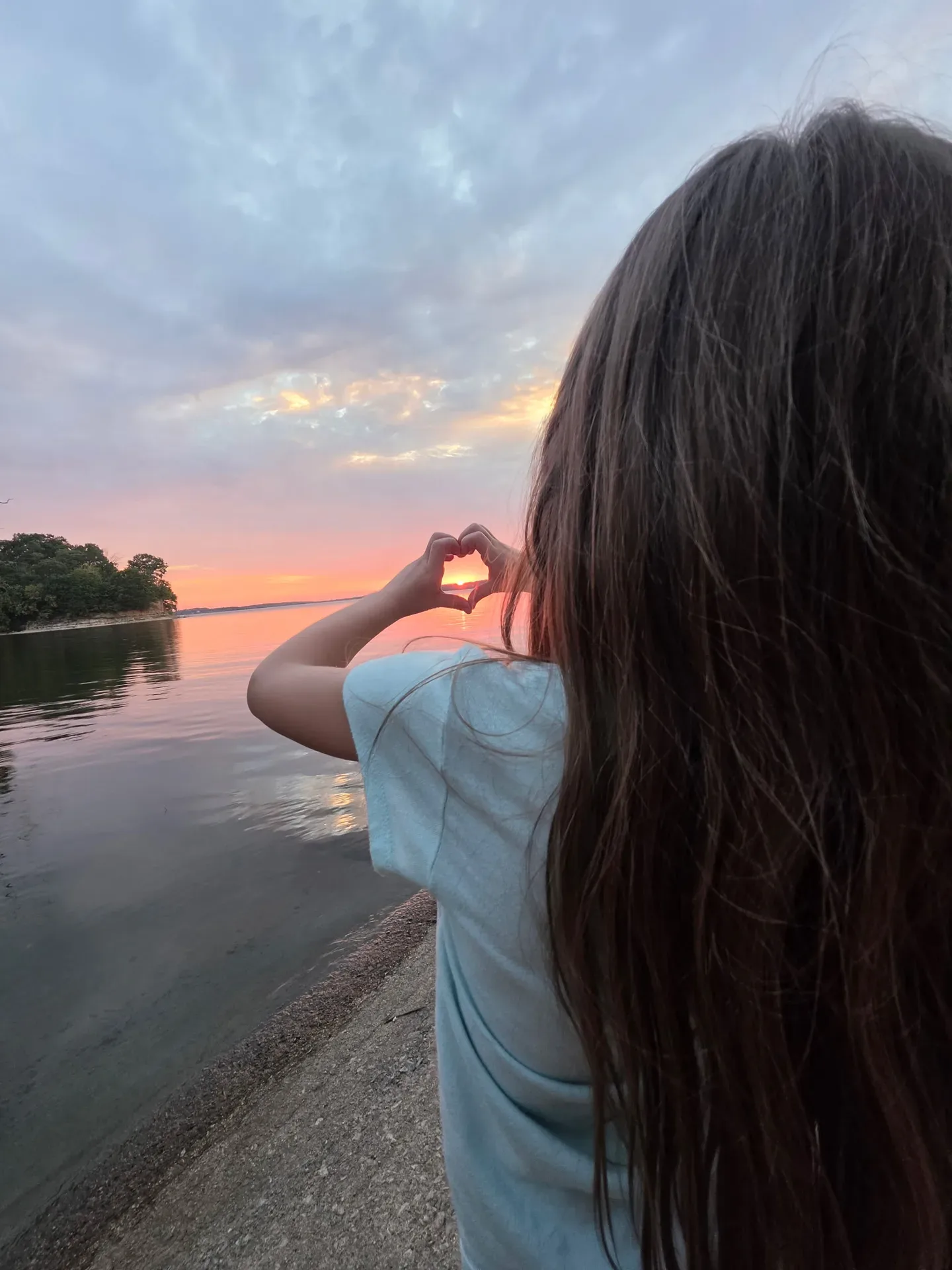 A person forms a heart with their hands around the sunset over Lake Hudson