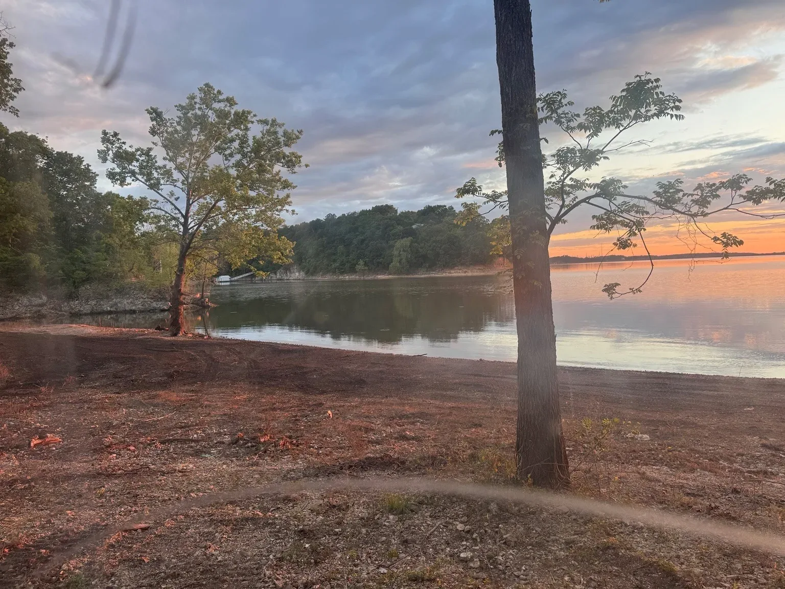 Quiet wooded shoreline of Lake Hudson at sunset with tree branches framing the water