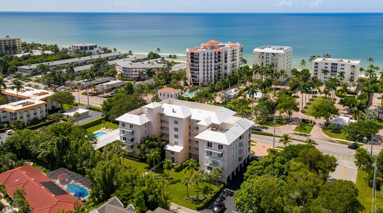 Aerial view of white coastal condominium complex in Coquina Sands with pools and ocean beyond
