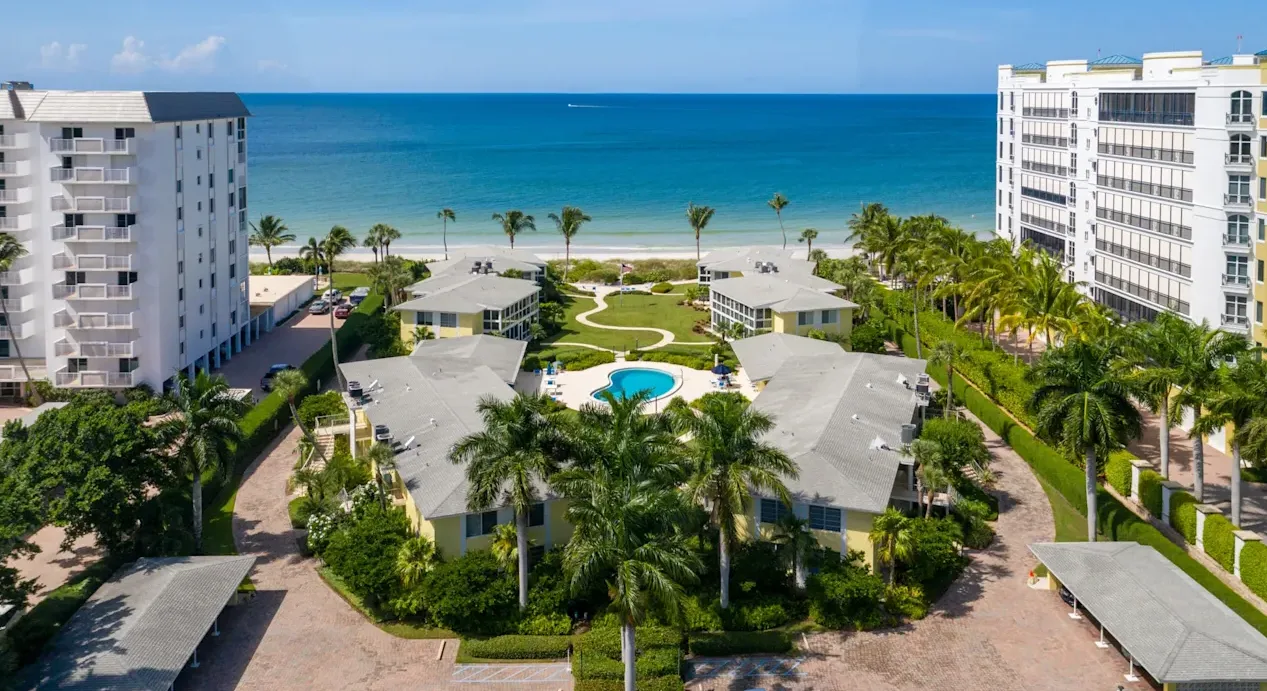 Drone aerial of tropical resort-style condo complex in Coquina Sands with pool, palm trees and beachfront