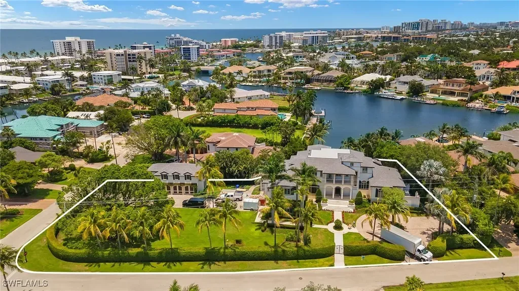 Elevated Naples waterfront estate on a large lawn with circular driveway and palm trees