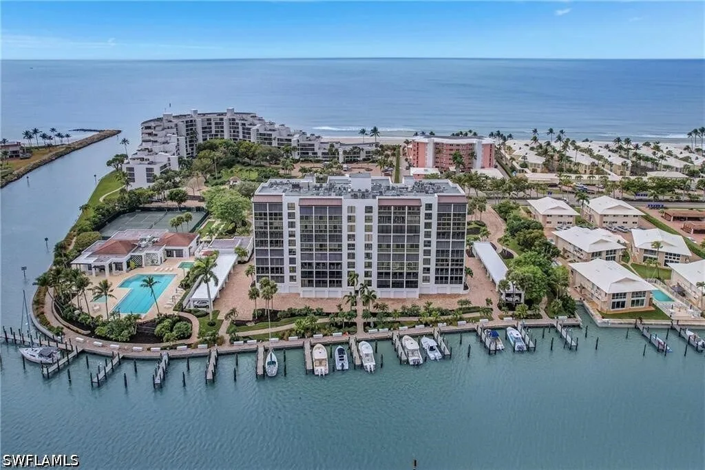 Drone view of a Naples beachfront community with pools, tennis courts, and boats docked behind the dune line