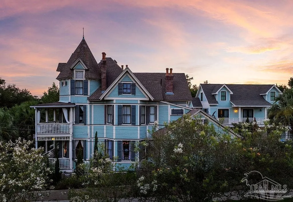The light blue Queen Anne Victorian estate at 714 E La Rua St glowing at sunset with its turret and gabled roofline.