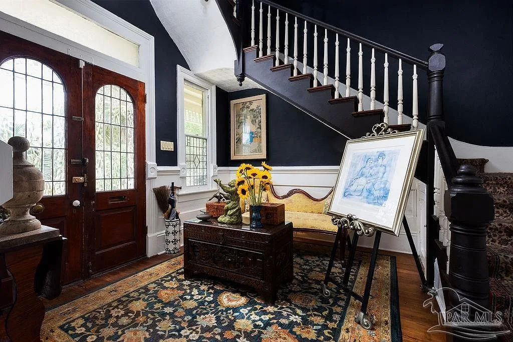 The grand entry foyer with dark navy walls, white wainscoting, a stained wood staircase, and the paned front door.