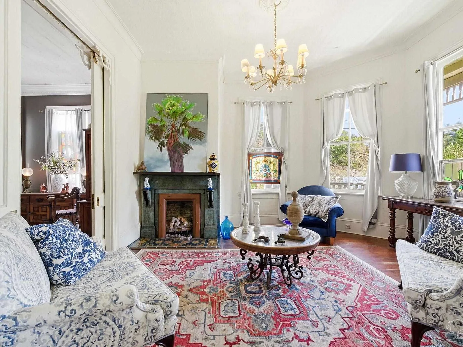 A Victorian parlor with an ornate fireplace surround, stained glass accents, and hardwood floors.