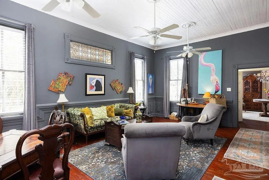 A grand wood-paneled Victorian living room with chair rail molding, tall windows, and gleaming floors.