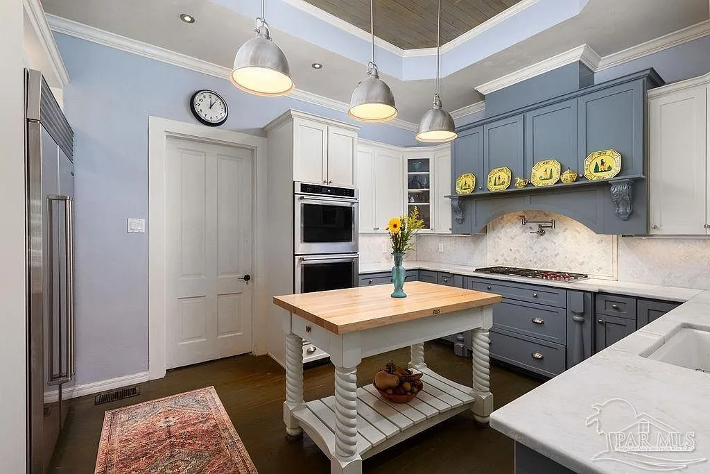 A chef's kitchen with grey and white cabinetry, marble countertops, stainless appliances, and a butcher-block island.