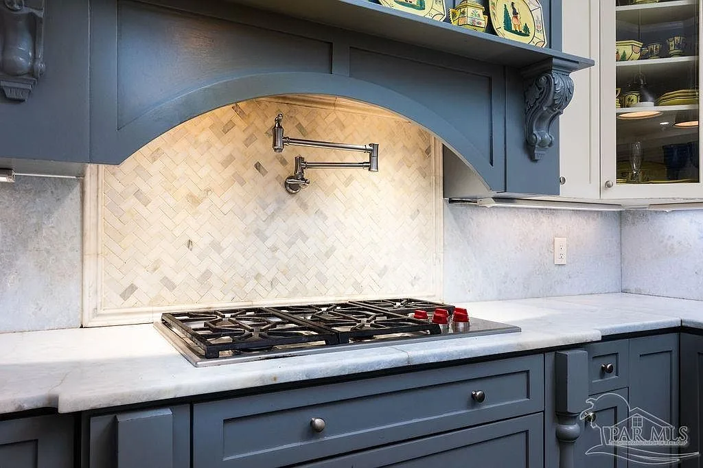 Detail of the cooktop with Victorian-inspired blue cabinetry, herringbone marble backsplash, and a wall-mounted pot filler.