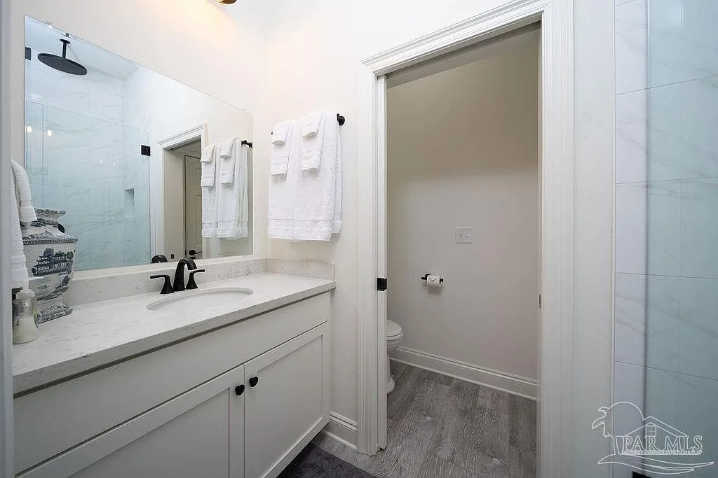 A clean modern bath with a white vanity, black fixtures, and a glass-enclosed shower.