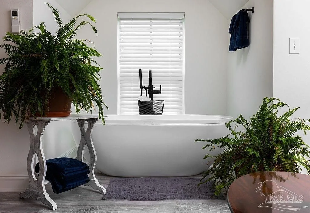 A freestanding soaking tub in a daylight-filled bath with black plumbing fixtures.