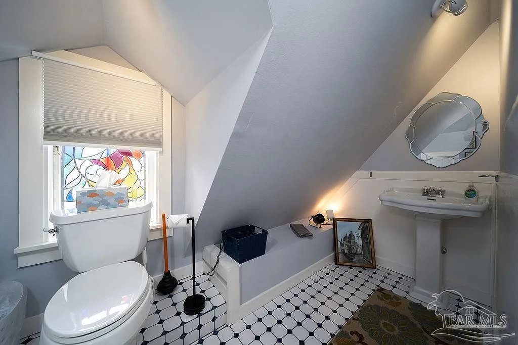 A historic attic bath with a white pedestal sink and a stained glass window.
