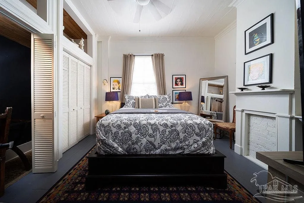 A high-ceilinged Victorian bedroom suite with a fireplace, louvered closets, and tall windows.