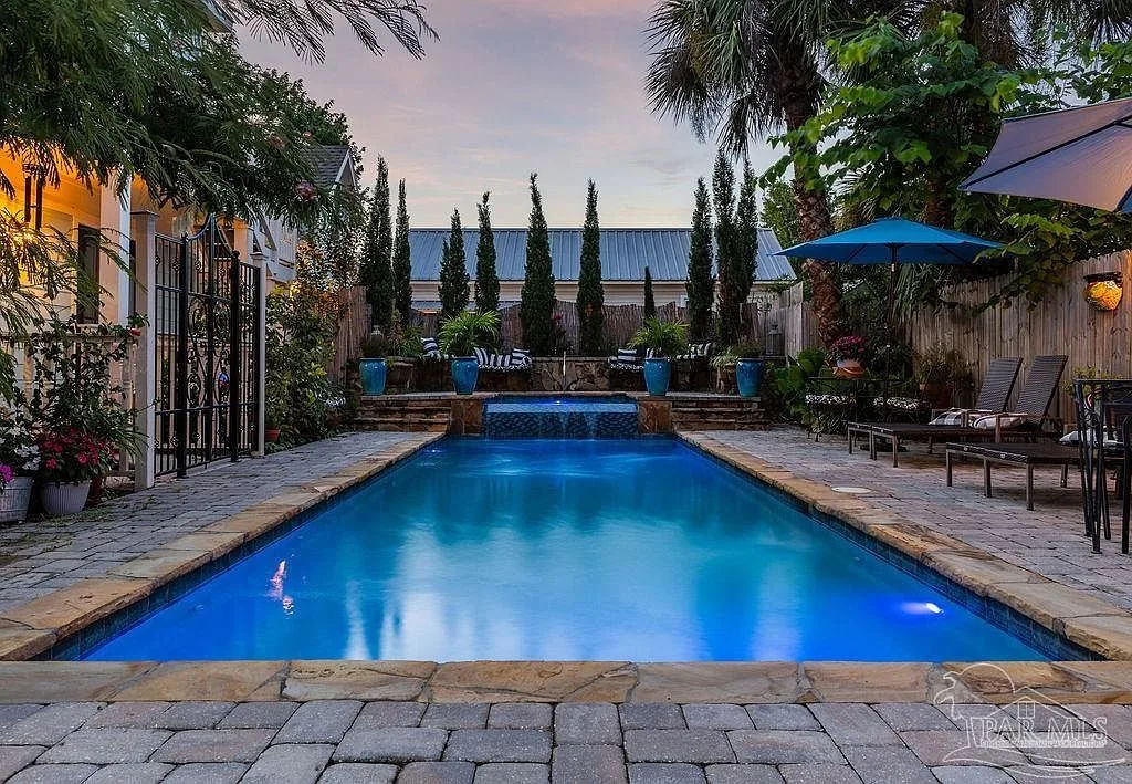 The courtyard at dusk with the saltwater pool, infinity spa, stone pavers, palms, and tall hedges.