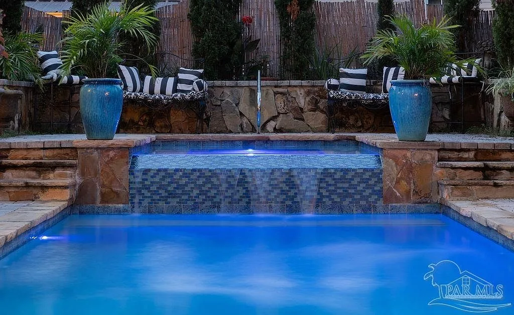 The stone-clad infinity spa with a waterfall cascading into the glowing blue pool at evening.
