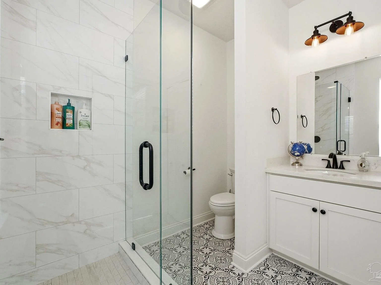 A marble-tile bath with a glass walk-in shower and black hardware.