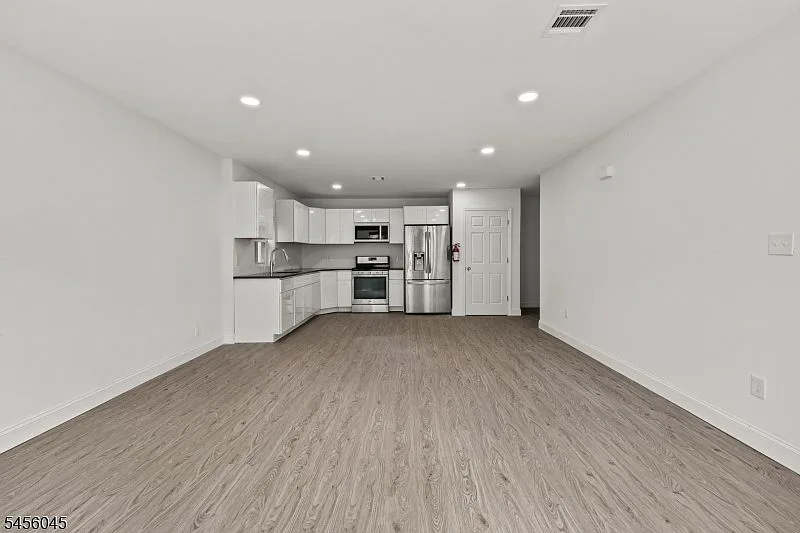 Open-concept kitchen and living area with white cabinetry, dark countertops, stainless steel appliances, and wood-look flooring.